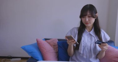 Oturma odasında elinde Card ve Smartphone olan bir Japon kadın. Yüksek kalite 4K görüntü. Tokyo Japonya 06.19.2025