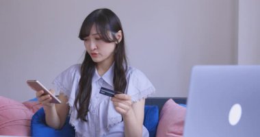 Oturma odasında elinde Card ve Smartphone olan bir Japon kadın. Yüksek kalite 4K görüntü. Tokyo Japonya 06.19.2025