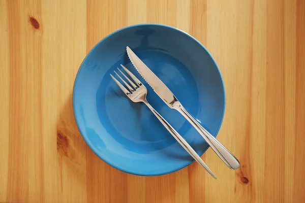 食事はボリュームがあり たくさんありました というシグナルがありました テーブルエチケットの例として 木製のテーブルの上にフォークとナイフで空ときれいな青のプレート — ストック写真