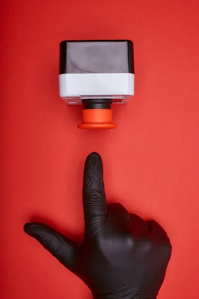 The hand in black vinyl glove, which pushes the emergency button at the red background at the side view
