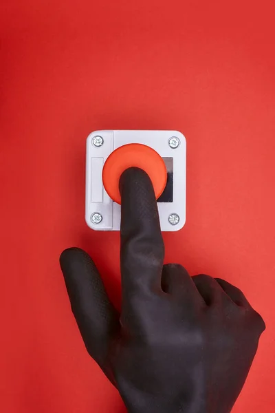 The hand in black vinyl glove, which pushes the emergency button at the red background at the top view