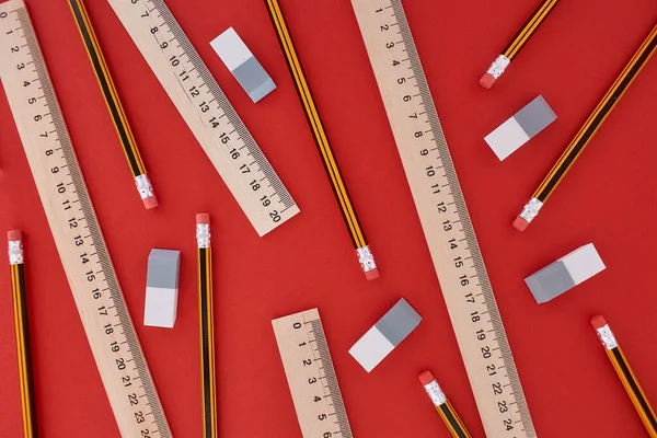 Randomly located many pencils, lines and erasers in top view at the red background