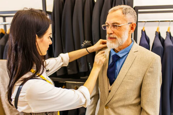 a professional tailor woman trying on a tailor-made suit for an elderly man.