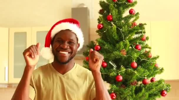 非洲裔美国人 戴着雪白的圣诞礼帽 望着自家圣诞树旁的照相机 — 图库视频影像