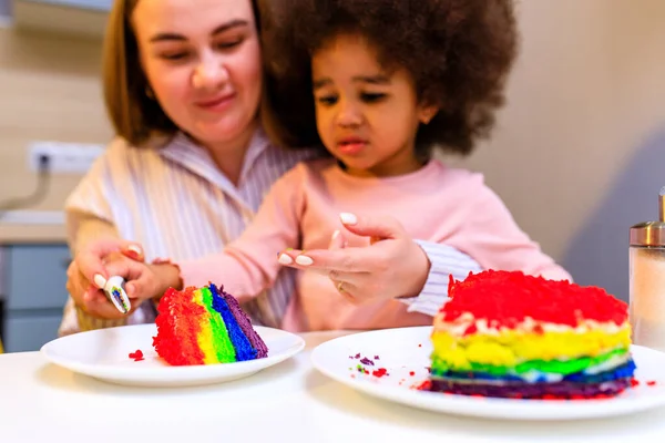 happy multiethnic family eating rainbow cake at kitchen .