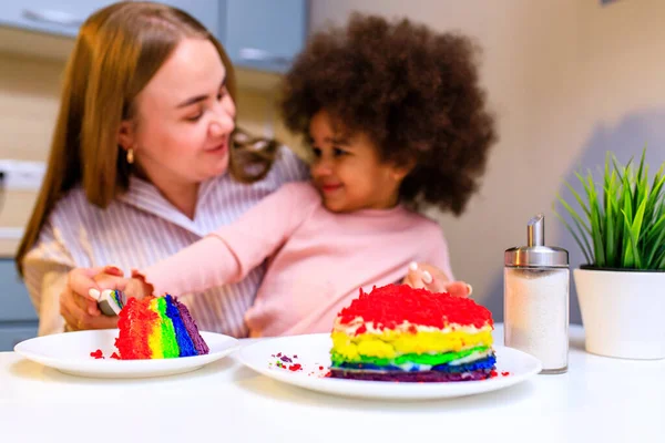 happy multiethnic family eating rainbow cake at kitchen .