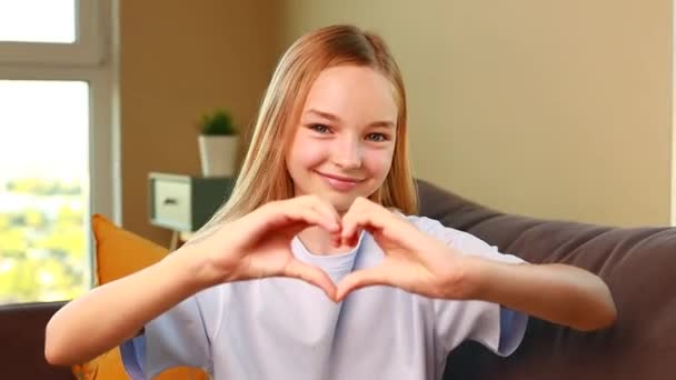 Щаслива Маленька Дівчинка Показує Жест Форми Серця Затишній Вітальні Вдома — стокове відео