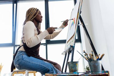 Resim stüdyosunda beyaz bluzlu, rastalı bir kadın..