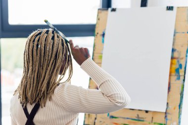 Afrika kökenli Amerikalı kadın çalışma alanında boş beyaz tuvalin yanında oturuyor..