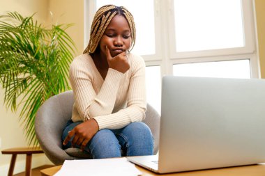 Latin Latin kadın kanepede oturuyor ve evdeki oturma odasında dizüstü bilgisayarla çalışıyor..