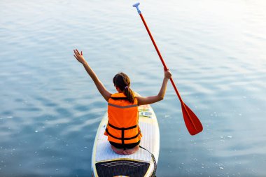 Hayat ceketli kadın nehir kenarındaki alt güvertede oturuyor. Orman ağaçları arka planda. .
