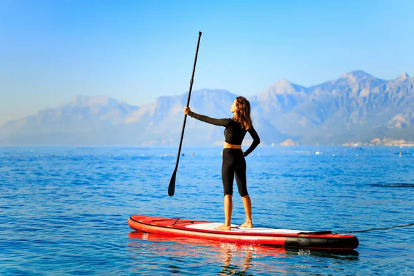 Woman paddling on sup board with mountains on background.