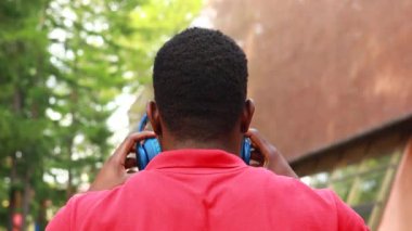 african american man in red t-shirt listening music in blue headphones and being in high spirit outdoors.