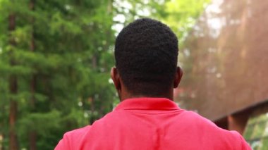 african american man in red t-shirt listening music in blue headphones and being in high spirit outdoors.