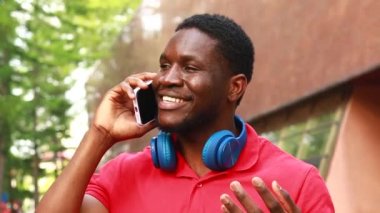 Genç Afro Amerikalı kulaklıklı adam yaz parkında akıllı telefon kullanıyor..