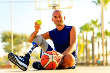 latin man with prosthetic leg sitting on coart and eating an apple. clipart