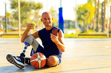 Tropikal deniz kenarında basketbol oynayan bacak protezi olan bir adam, zirve zamanında elma yiyor..