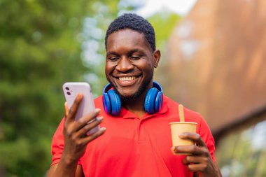 Genç Afro Amerikalı kulaklıklı adam yaz parkında akıllı telefon kullanıyor. .