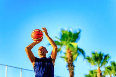 Türk adam yaz günü dışarıda basket oynuyor. Mavi gökyüzü arka planında. .