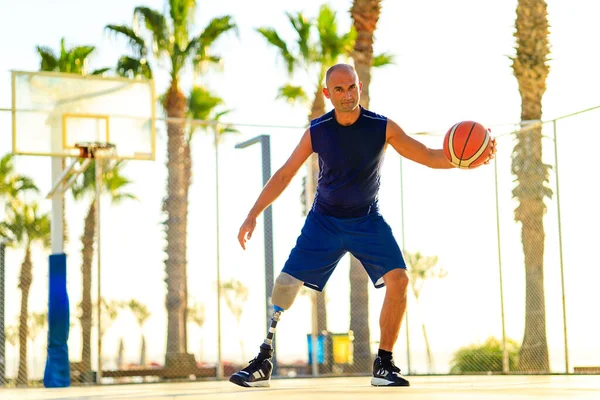 sporty handicapped man in sportswear and with artificial leg basketball player at sunset.