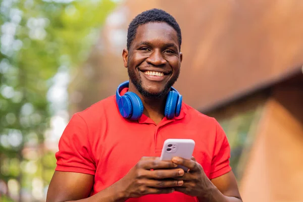 stock image young afro american man with headphones on neck using smartphone in summer park .