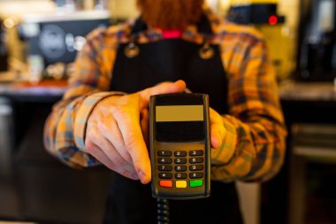 Profesyonel barista, kızıl saçlı, sakallı, siyah önlüklü, kafede çalışan genç bir adam..