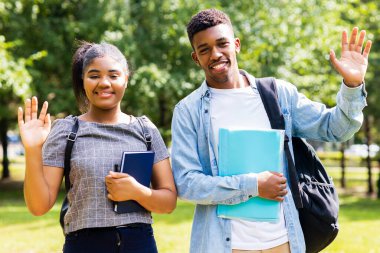 Afro-Amerikalı arkadaşlar güneşli bir günde parkta üniversite kampüsünde bilgi paylaşıyorlar..