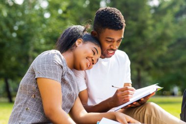 Afro-Amerikalı arkadaşlar güneşli bir günde parkta üniversite kampüsünde bilgi paylaşıyorlar..