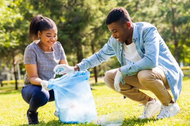 Afrika kökenli Amerikalı gönüllüler güneşli yaz parkında plastik çöp topluyorlar..