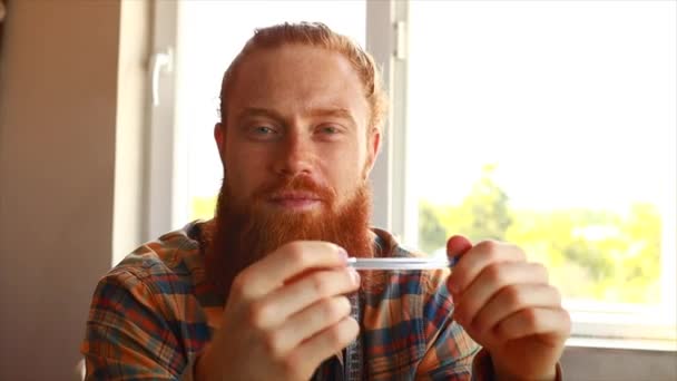 長い髭を生やしたハンサムな赤毛の男は自宅のスタジオでミシンで縫う — ストック動画