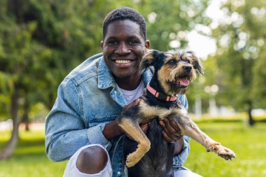 Latin Amerikalı adam güneşli bir günde sevimli köpeğiyle çimlerin üzerinde çimlerin üzerinde yürüyor..