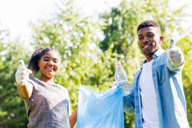 Afrika kökenli Amerikalı gönüllüler güneşli yaz parkında plastik çöp topluyorlar..