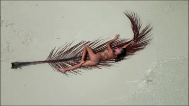 Güneş banyosu yapan genç bir kadın kumsalda beyaz bir kumsalda bikini giyiyor..