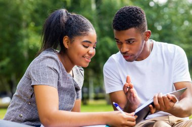 Afro-Amerikalı arkadaşlar güneşli bir günde parkta üniversite kampüsünde bilgi paylaşıyorlar..