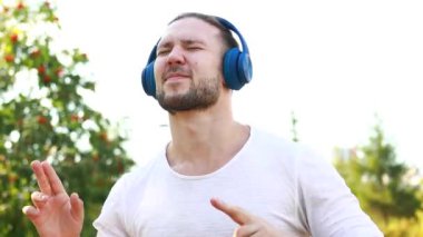Mutlu adam kulaklıkla müzik dinliyor açık havada beyaz ceketli yaz parkında.
