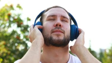 Mutlu adam kulaklıkla müzik dinliyor açık havada beyaz ceketli yaz parkında.