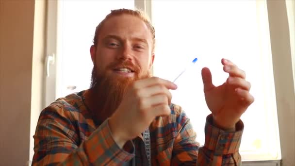 長い髭を生やしたハンサムな赤毛の男は自宅のスタジオでミシンで縫う — ストック動画