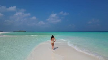 Güneş banyosu yapan genç bir kadın kumsalda beyaz bir kumsalda bikini giyiyor..