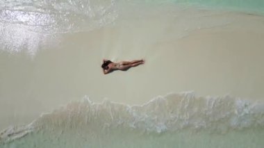 Güneş banyosu yapan genç bir kadın kumsalda beyaz bir kumsalda bikini giyiyor..