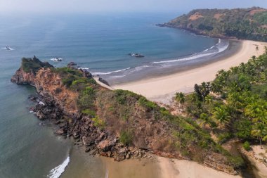 Goa 'da güneş ışığı altında yeşil palmiye ağaçlarıyla tropikal plajda hava manzarası.