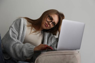 Üzgün genç bir kadının, oturma odasındaki kanepede oturup dizüstü bilgisayarına baktığı yakın çekim. Mavi ışıklı gözlüklü, elleri klavyede mutsuz bir kadın. Boşluğu kopyala, arkaplan.