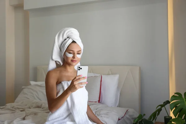 Young woman wearing a towel after showering recording a video review of the under eye patch for dark circles treatment for her beauty blog. Close up, copy space, background.