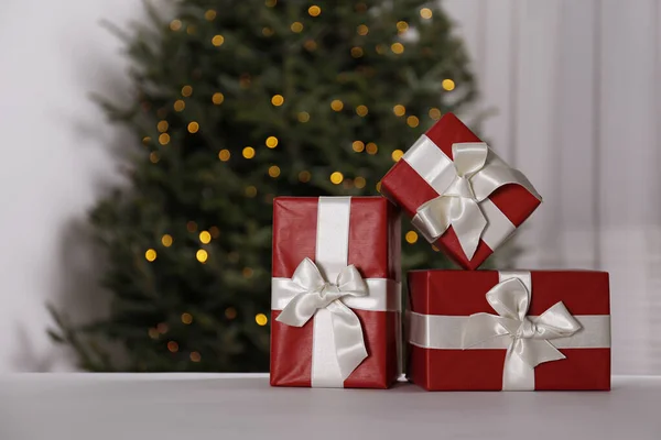 Close up shot of three presents. Christmas tree decorated with soft yellow lights, bokeh effect background. Traditional new year holiday decoration, intimate lighting. Close up, copy space.