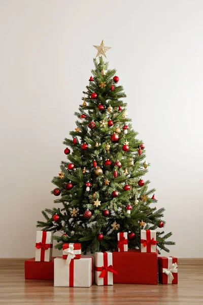 光沢のある泡と木製の床に多くの異なるプレゼントで飾られた大きな美しいクリスマスツリー テキストのための多くのコピースペースを持つ白い壁の背景 閉じろ ロイヤリティフリーのストック写真