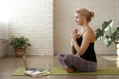 Sporty adult woman teaching yoga in an online class. Fit middle aged yogini live streaming a meditation. Copy space, close up, white brick wall background.