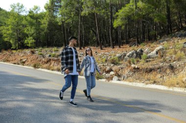 Flanel gömlekli mutlu hippi çiftin olduğu romantik bir sahne. Boş arka yolda yürüyorlar. El ele tutuşan gençler. Kapat, kopyala boşluk, arkaplan.