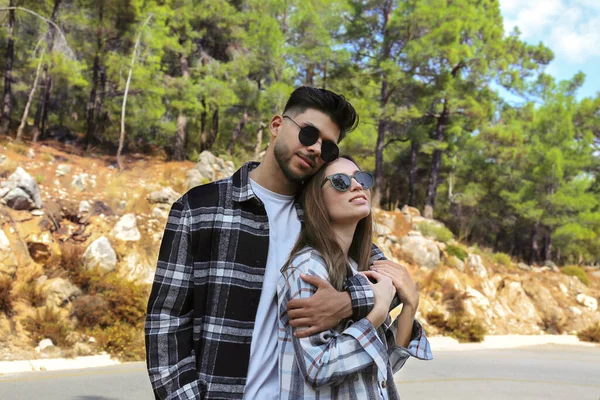 Portrait of a hipster couple in casual outfit hugging outdoors. Happy young people wearing checked flannel shirts and sunglasses on a hiking trail in the woods. Close up, copy space.