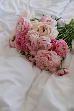 A beautiful bouquet of peonies and ranunculus flowers on the empty unmade bed with white sheets. A romantic surprize for st. Valentine's day. Close up, copy space, background, top view, natural light