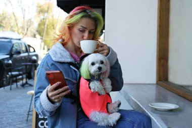 Genç bir kadın, evcil hayvan taşıyıcı çantasında köpeğiyle sabah kahvesinin tadını çıkarıyor. Kapat, kopyala boşluk, arkaplan.