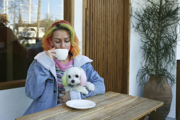 Young woman enjoying the morning cup of coffee with her maltese dog in a pet carrier backpack. Close up, copy space, background.